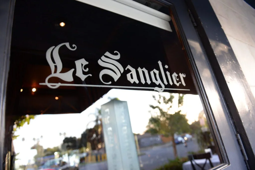 Le Sanglier storefront sign with ornate lettering on dark background and window reflection