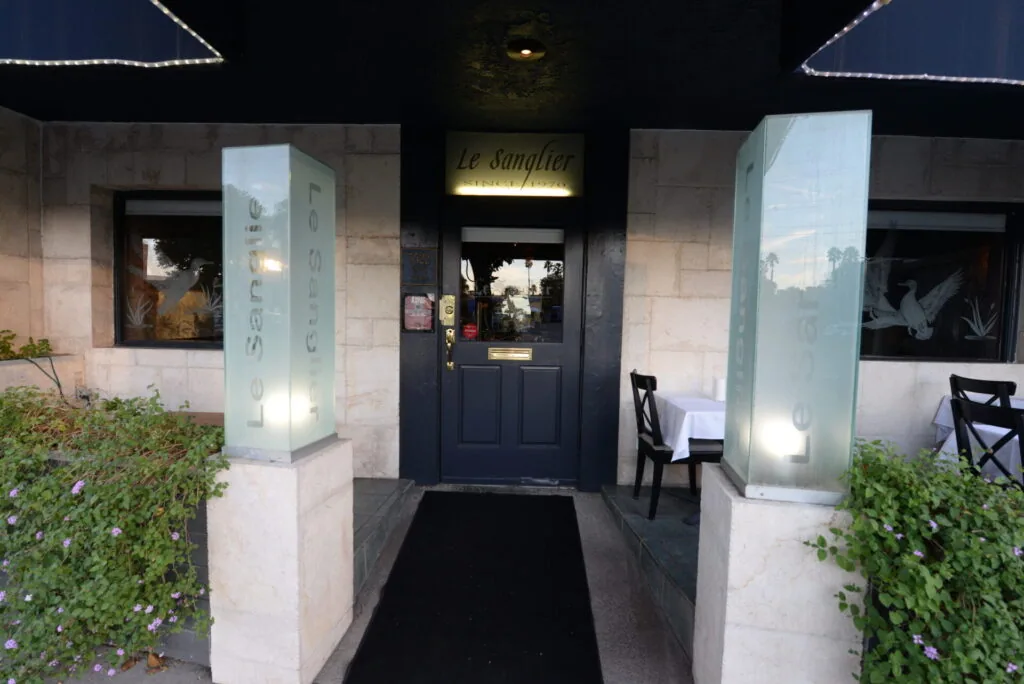 Restaurant entrance at night with dark blue door, illuminated planters, and climbing ivy on either side