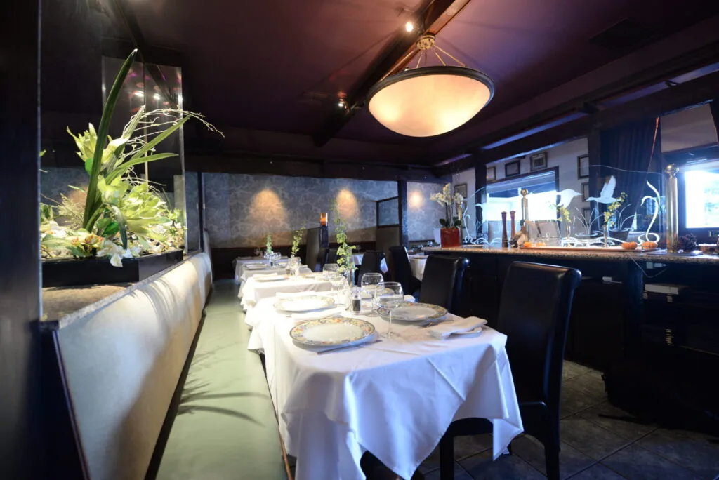 Upscale restaurant dining room with white tablecloths, illuminated aquarium, pendant lighting, and modern decor