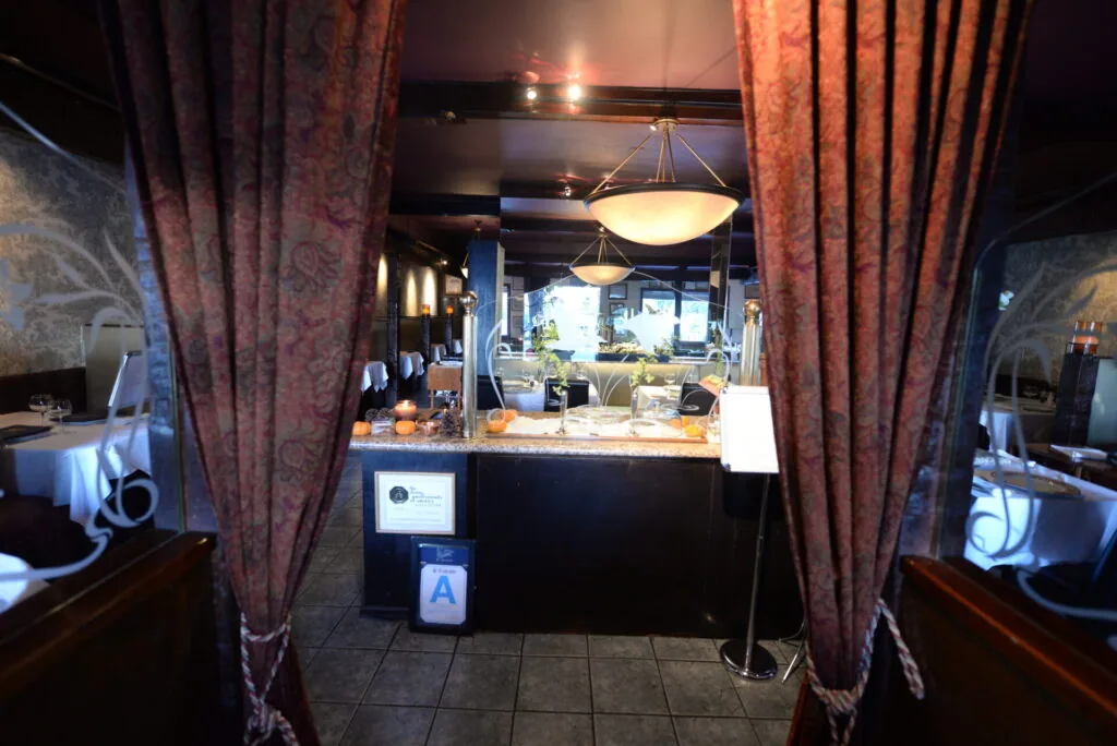 Restaurant entrance with burgundy curtains framing a black counter desk beneath a pendant light fixture