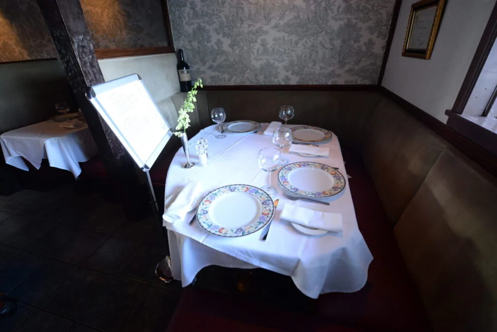 Fine dining table set with white linens, decorative plates, glassware, and a floral centerpiece in an intimate restaurant booth