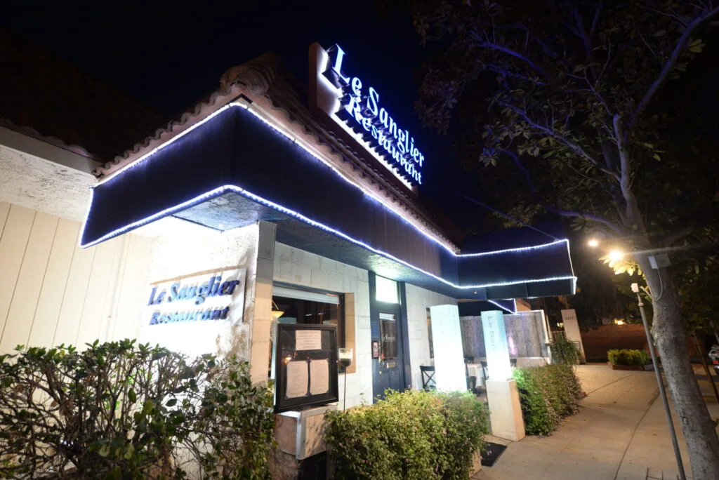 Nighttime storefront with blue neon outline lighting and signage for Le Sanglier restaurant