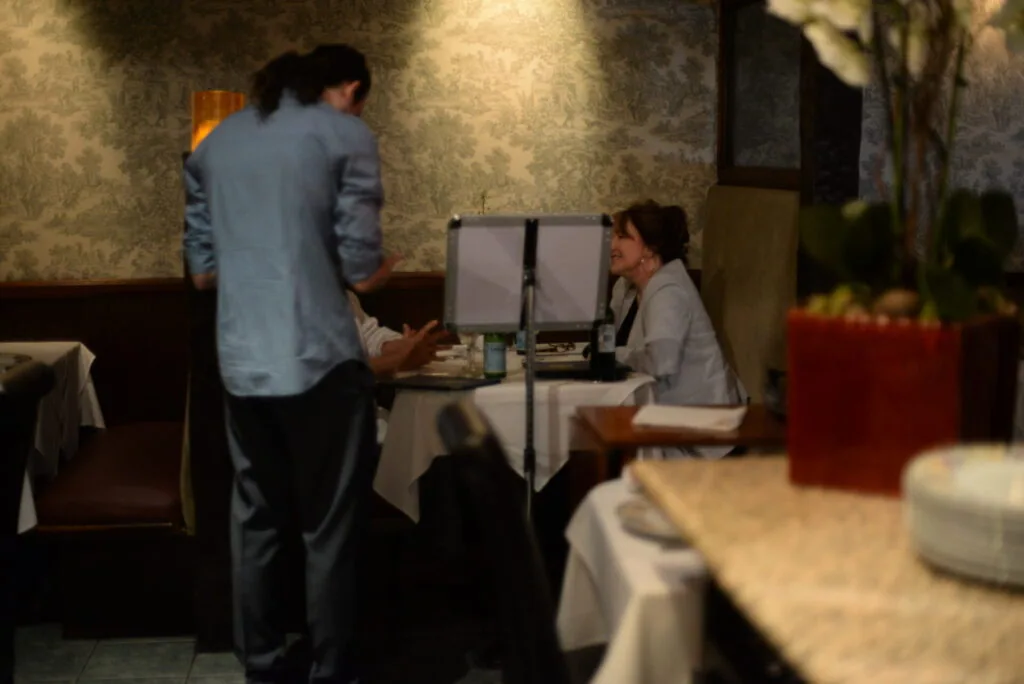 Two people at a restaurant reception desk with a computer monitor between them