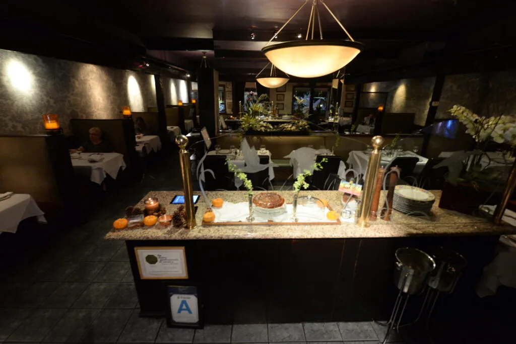 Fine dining restaurant interior with black bar, granite countertop, pendant lighting, white tablecloths, and floral arrangements