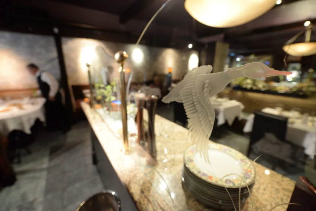 White ceramic flying bird figurine on a dining table with table settings and warm overhead lighting in an upscale restaurant