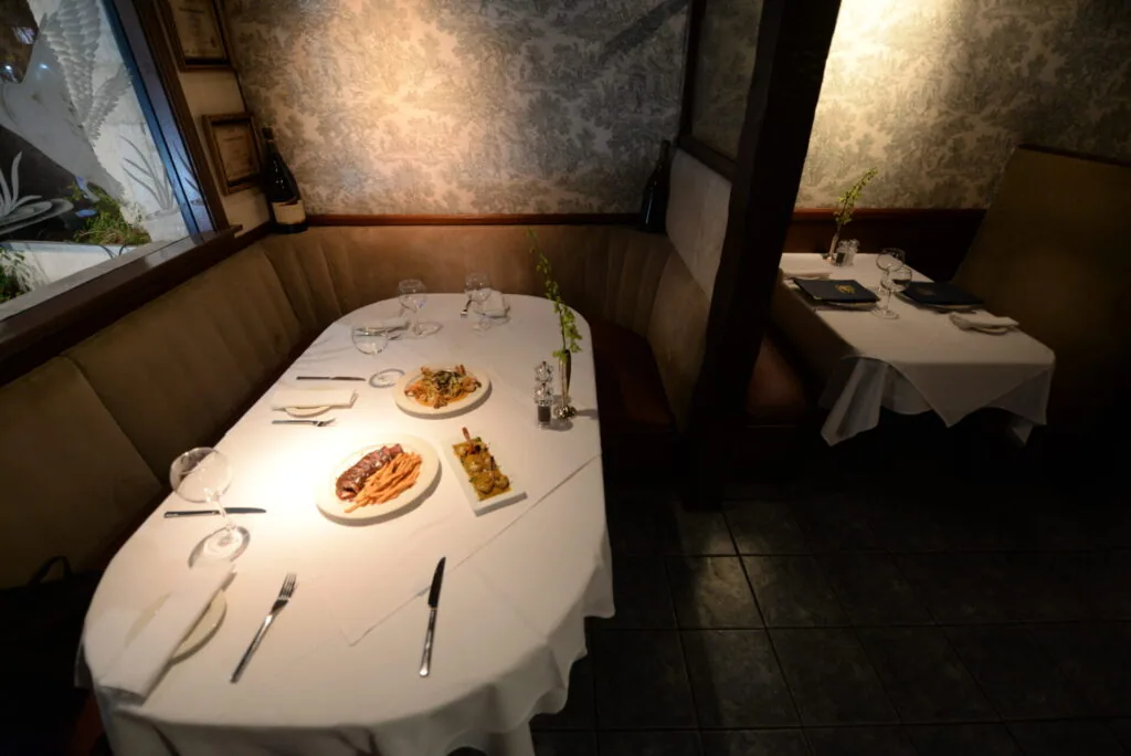 Fine dining booth with white tablecloth, plated dishes, place settings, and glassware in an upscale restaurant interior