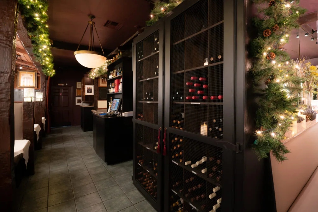 Upscale wine bar interior with dark wood cabinetry, illuminated bottle displays, and festive garland with warm lights