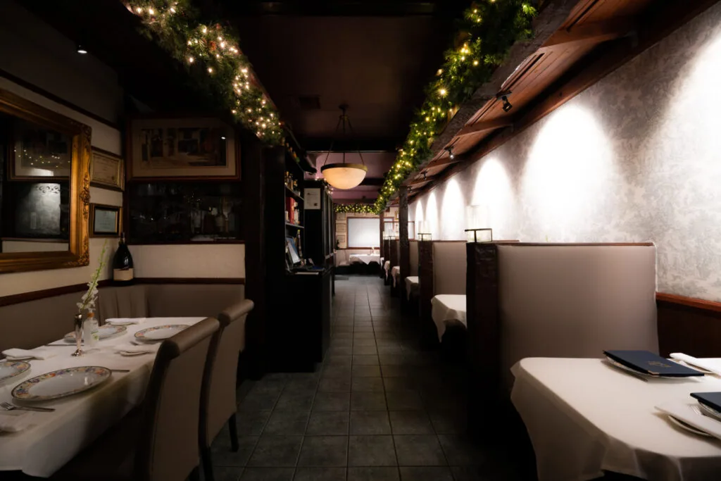 Restaurant interior with booth seating along walls, festive garland lighting overhead, and framed artwork on walls