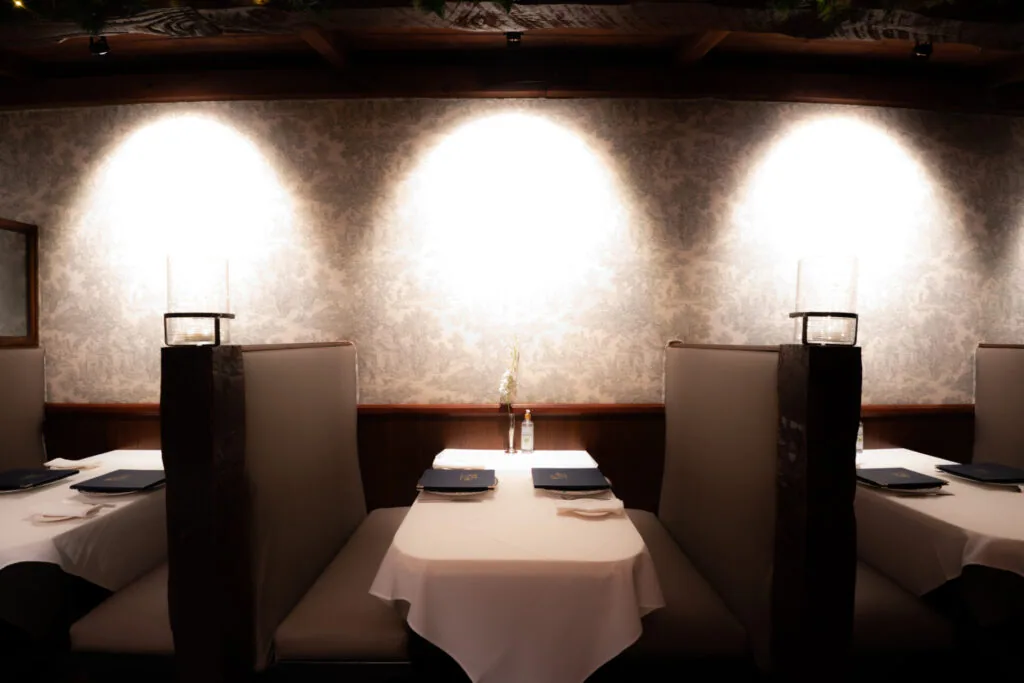Fine dining restaurant interior with white tablecloth tables, high-back booth seating, and three round uplights on textured wall