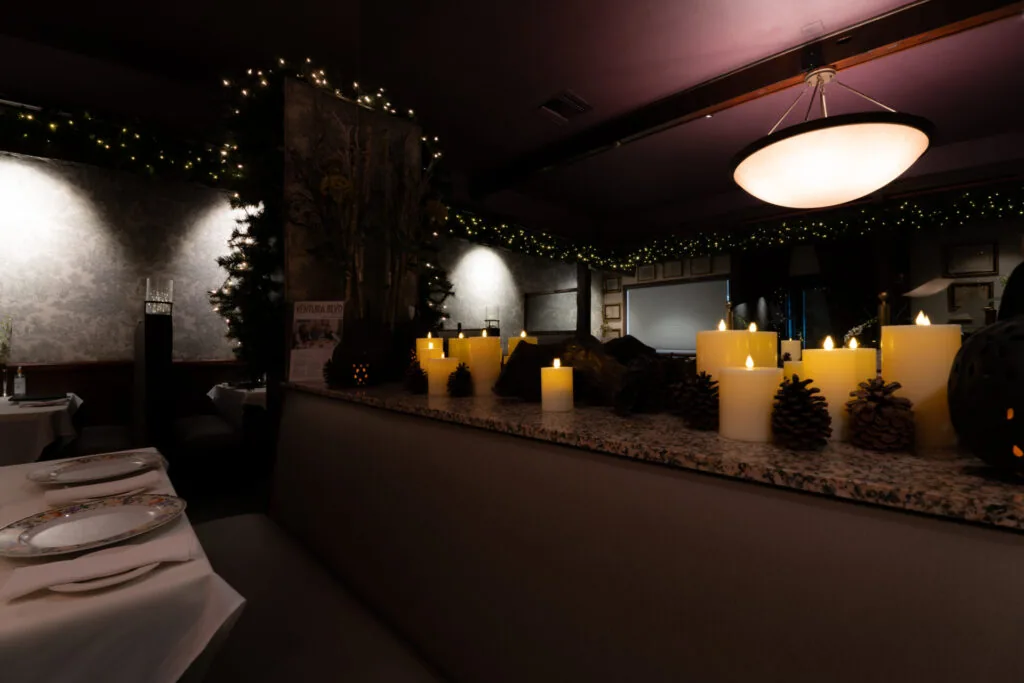 Elegant dining room with large glowing candles, hanging pendant light, festive garland, and formal table settings