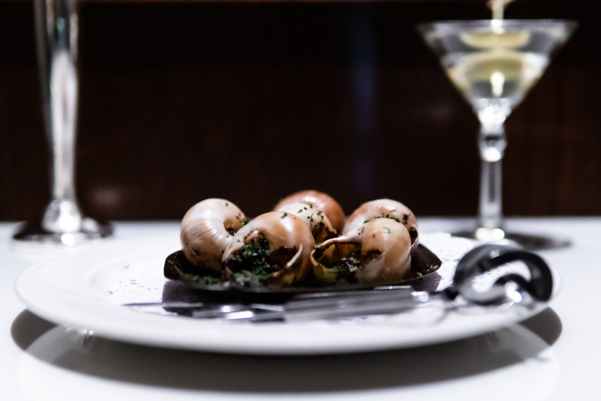 Escargot in garlic butter beside a martini, on a candlelit table at Le Sanglier