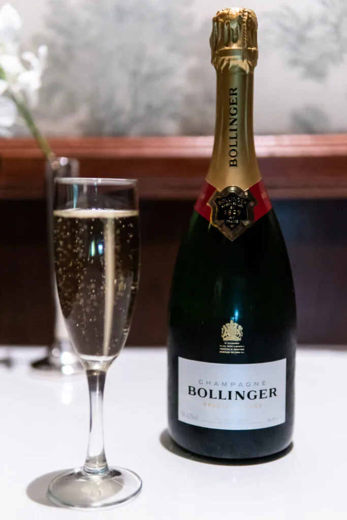 Champagne bottle with gold foil and red label next to a filled champagne glass with bubbles, windowed background