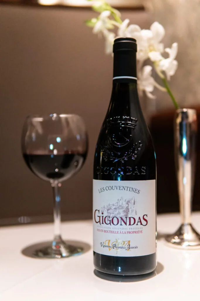 Bottle of Gigondas red wine with a glass of wine and white flowers in background