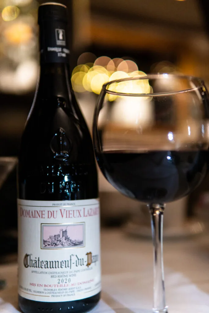 Red wine bottle and filled wine glass on table with warm bokeh lighting in background