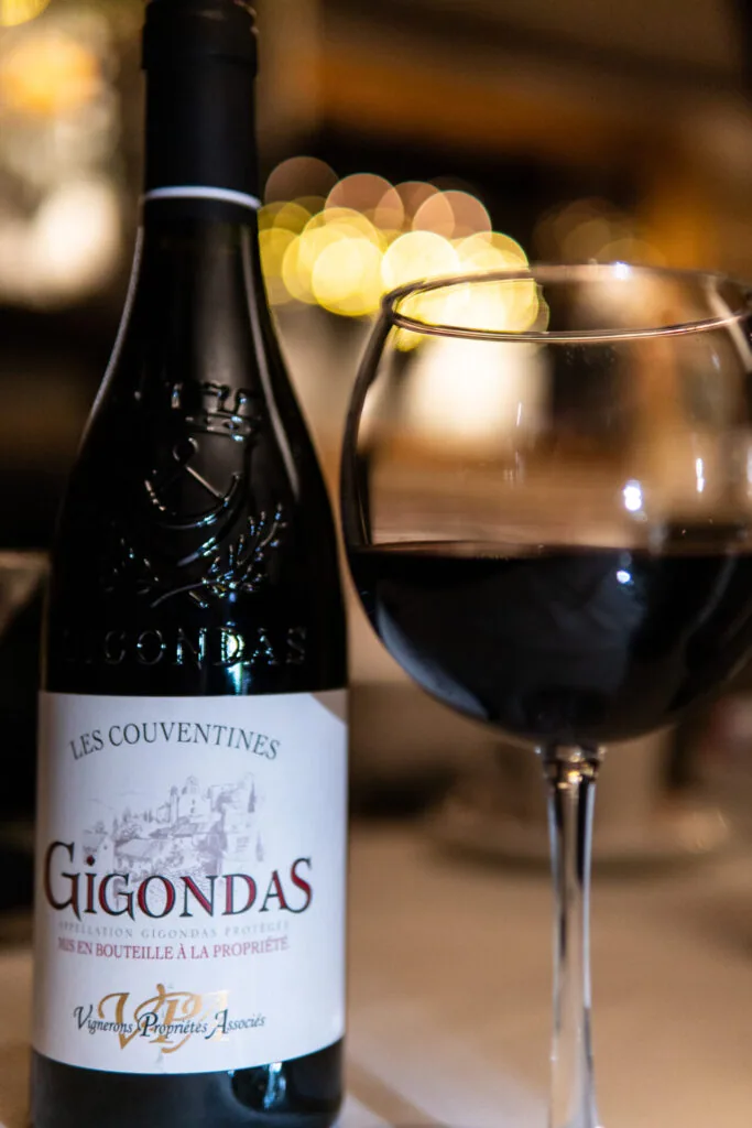Red wine bottle and filled wine glass with warm bokeh lights in background