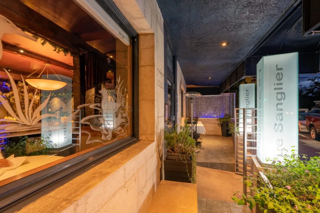 Modern storefront entrance at night with illuminated window display, potted plants, and signage reading 'Sanglier'