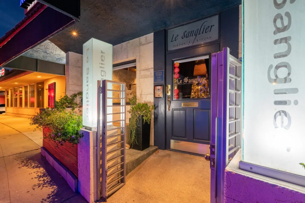 Nighttime storefront with purple neon accents, metal gate entrance, and signage reading 'Le Sanglier'