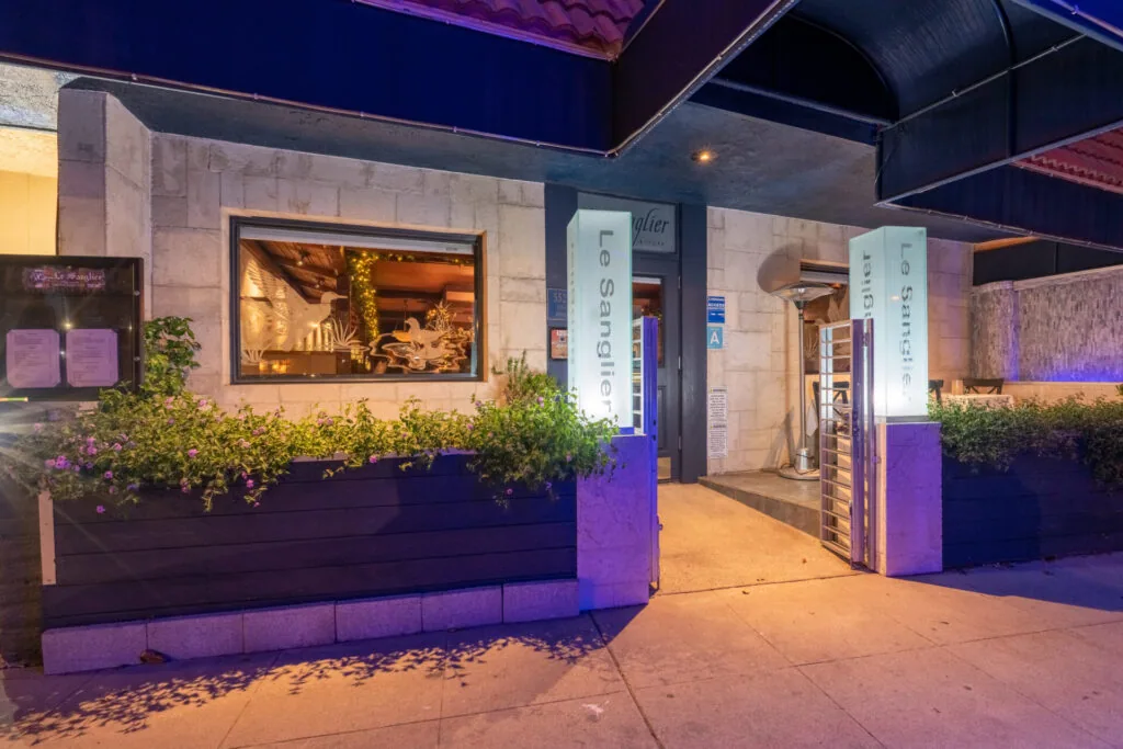 Restaurant storefront with illuminated window display, purple planters with greenery, and dark entrance at night